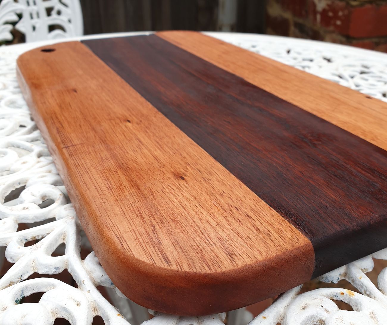 A two-tone timber board with a dark centre stripe and a hanging hole