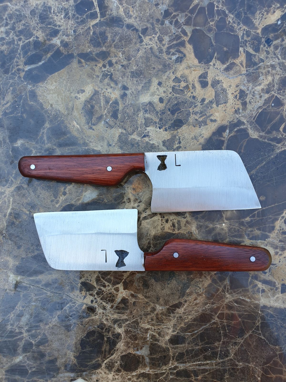 Two mini cheese cleavers with timber handles, each stamped with an L and a small hourglass