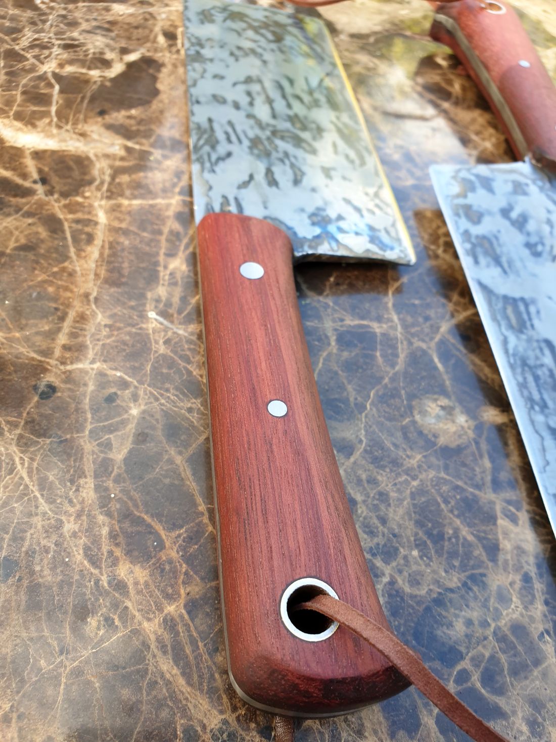 Close-up of a timber cleaver handle with steel pins and a leather lanyard