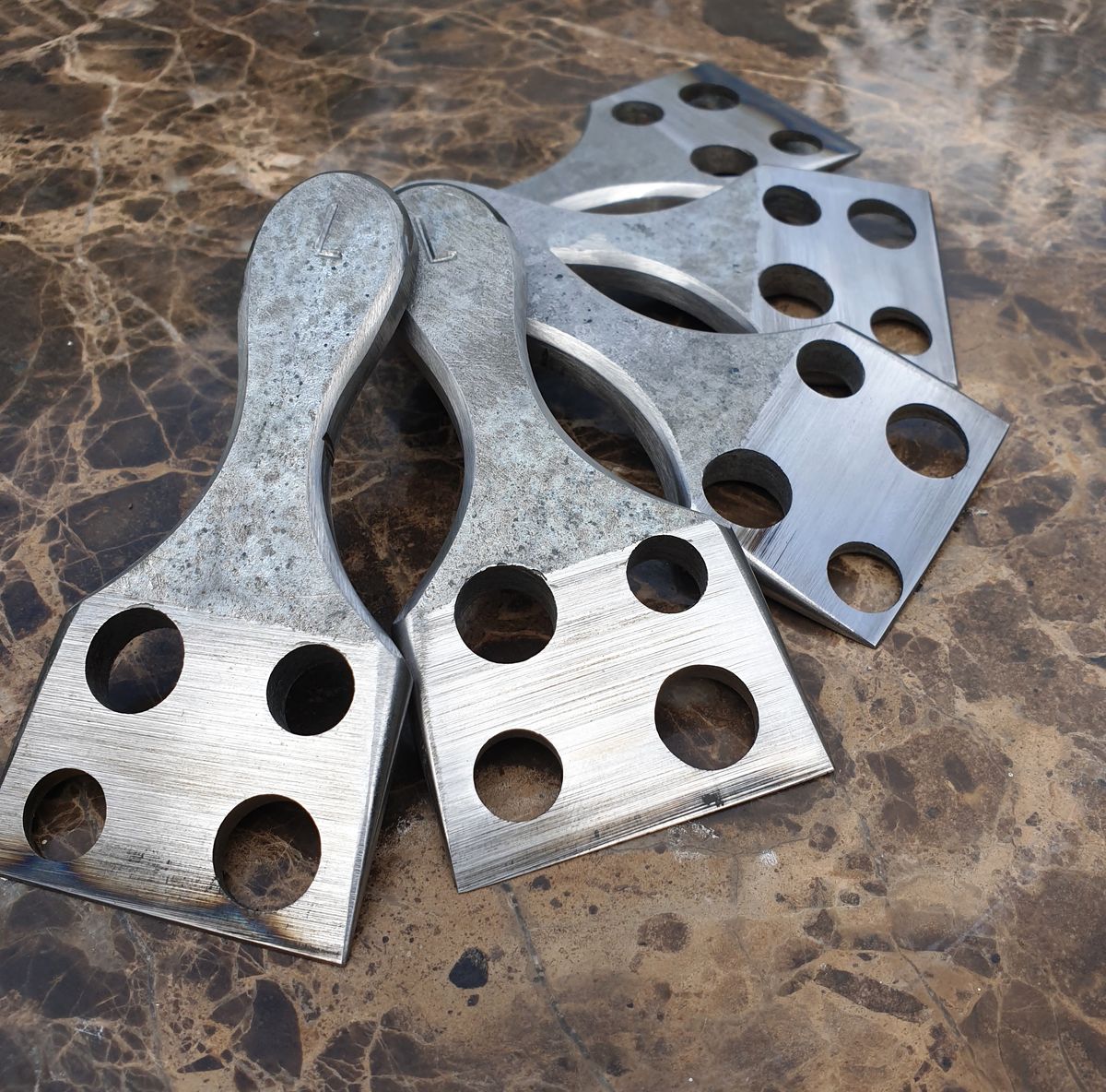 A stack of steel cheese choppers with drilled holes on a marble bench, two stamped with an L