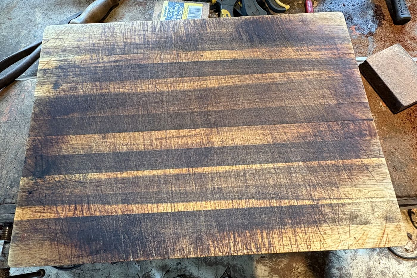 A timber chopping board before restoration: dark, stained and covered in knife marks