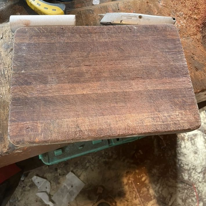 A worn timber chopping board on a workbench before restoration