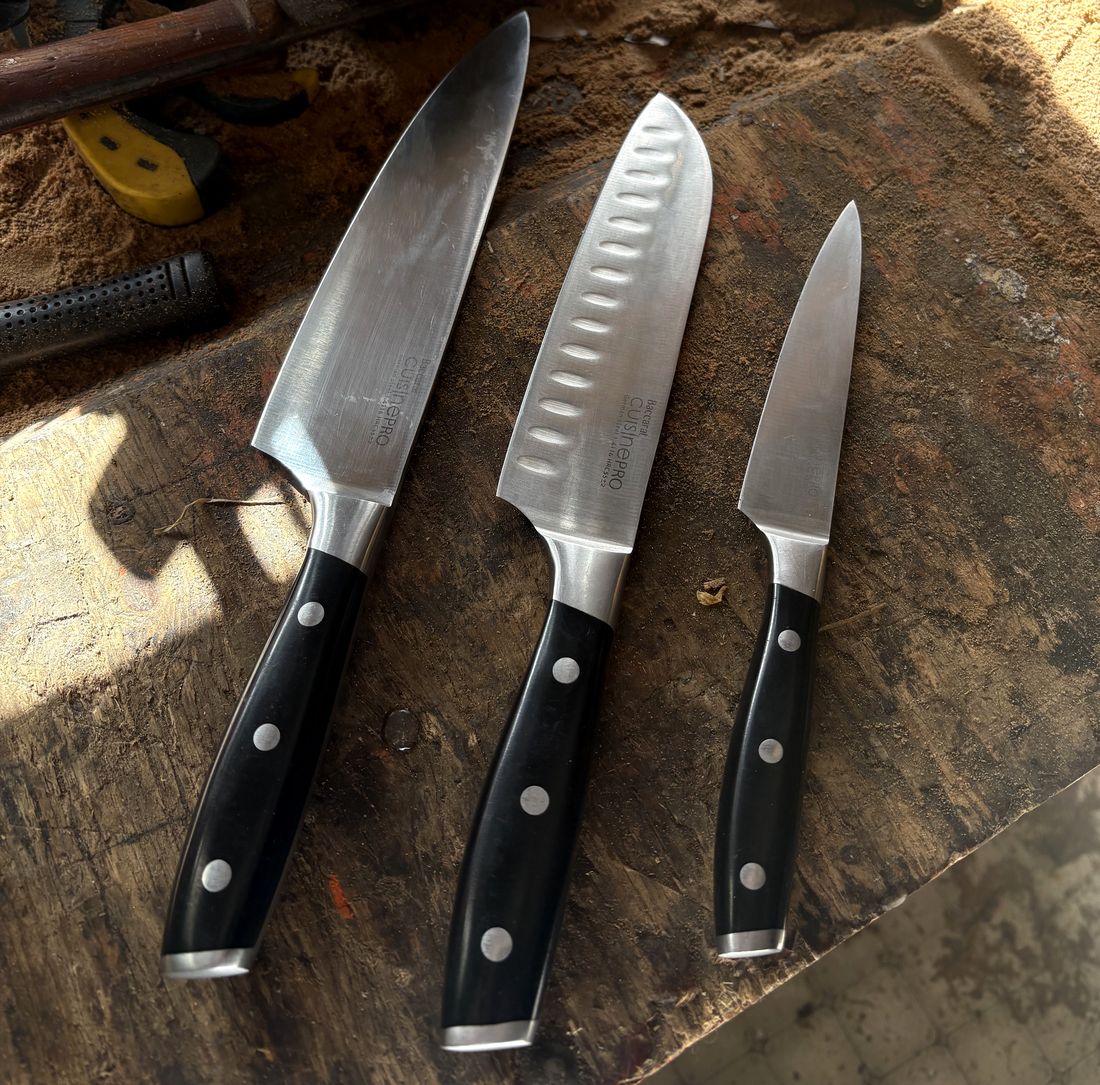 A chef's knife, santoku and paring knife with black handles on a workbench
