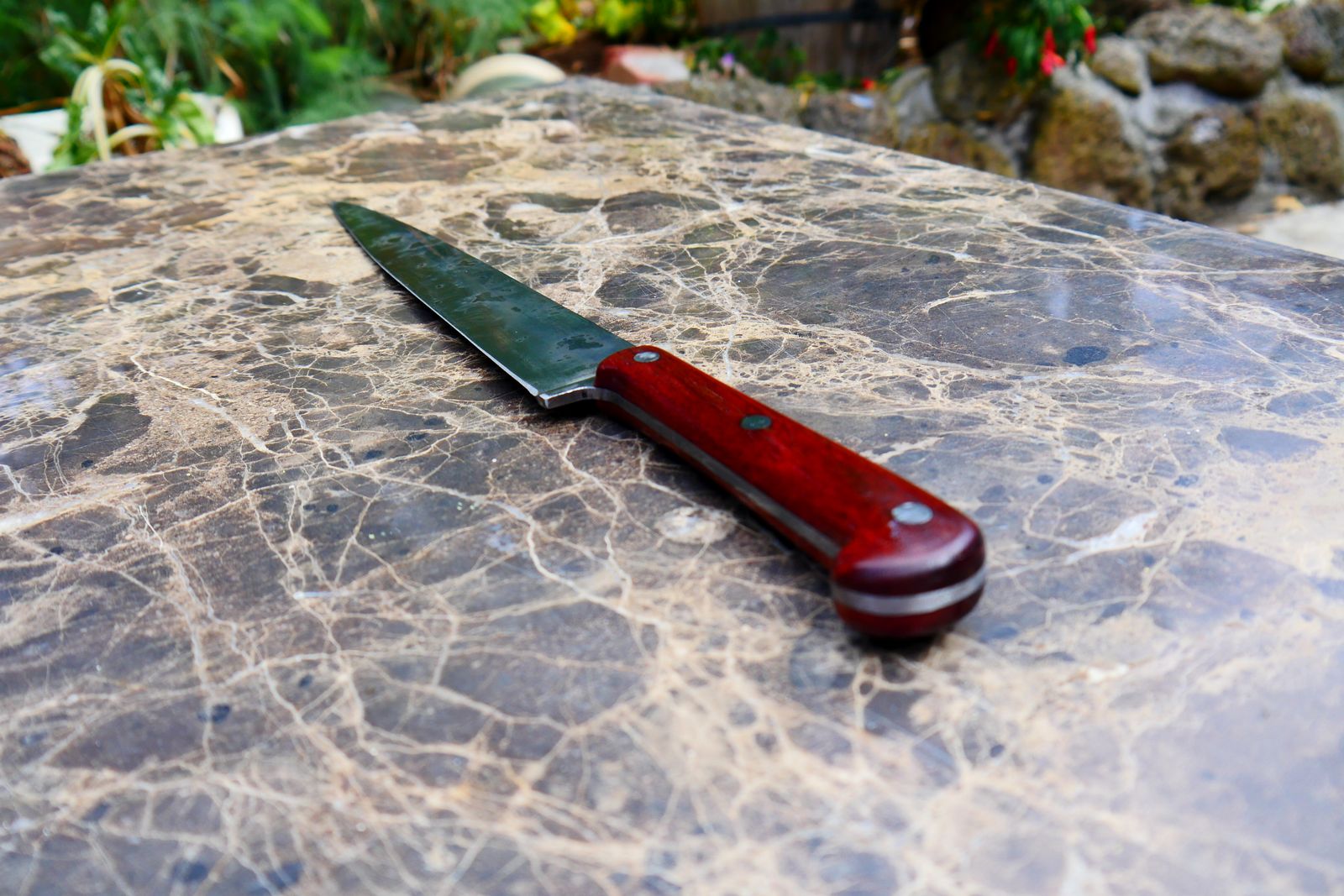 A handmade slicing knife with a red timber handle on a marble bench