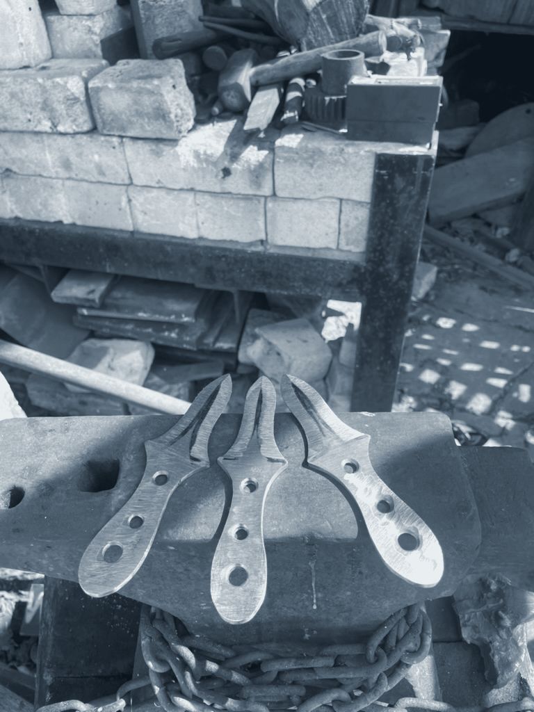 Three shaped and drilled knife blanks on an anvil